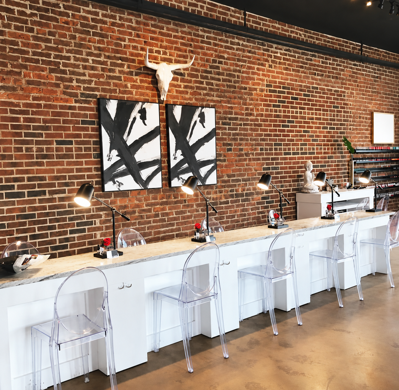 Manicure stations with clear chairs and an exposed brick wall at the Columbia studio
